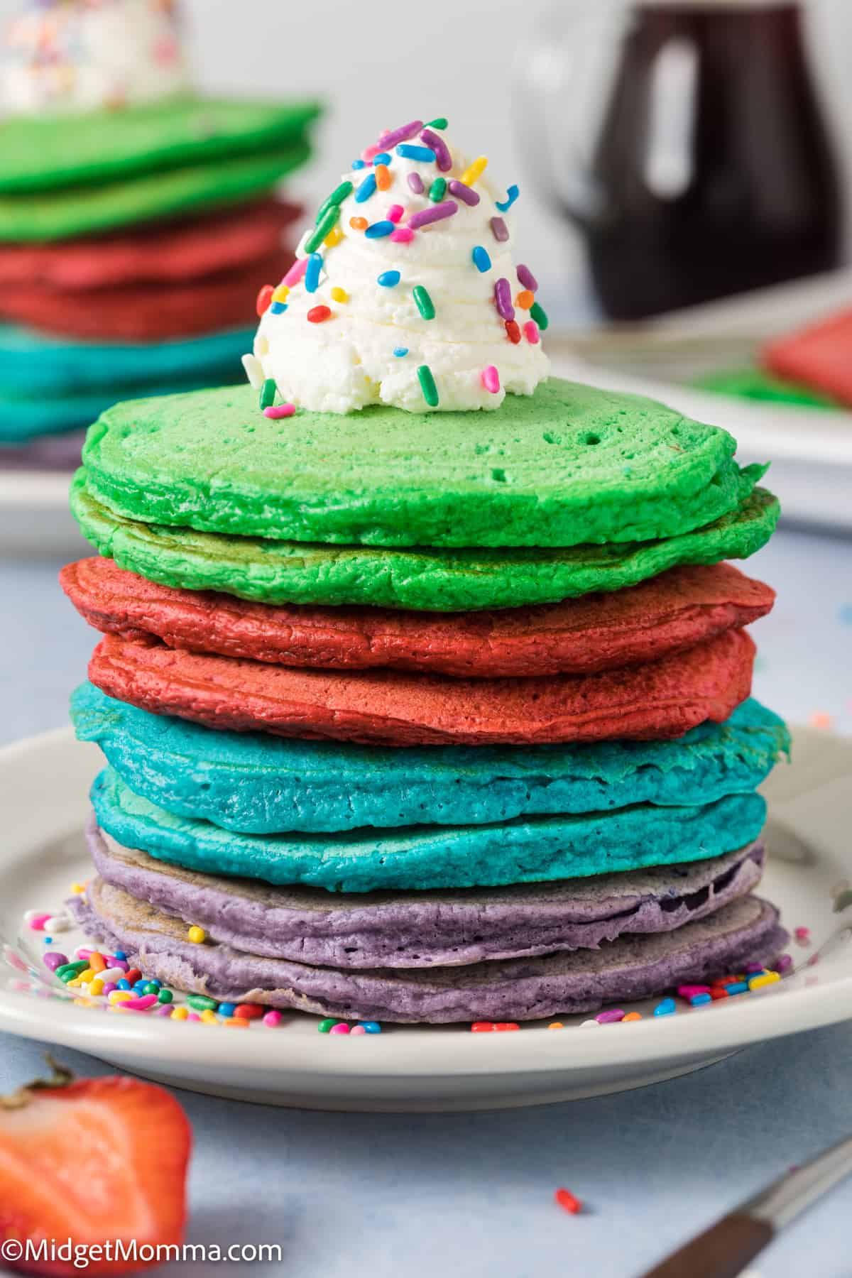 close up photo of a stack of rainbow pancakes - 2 green pancakes, 2 red pancakes, 2 blue pancakes, 2 purple pancakes