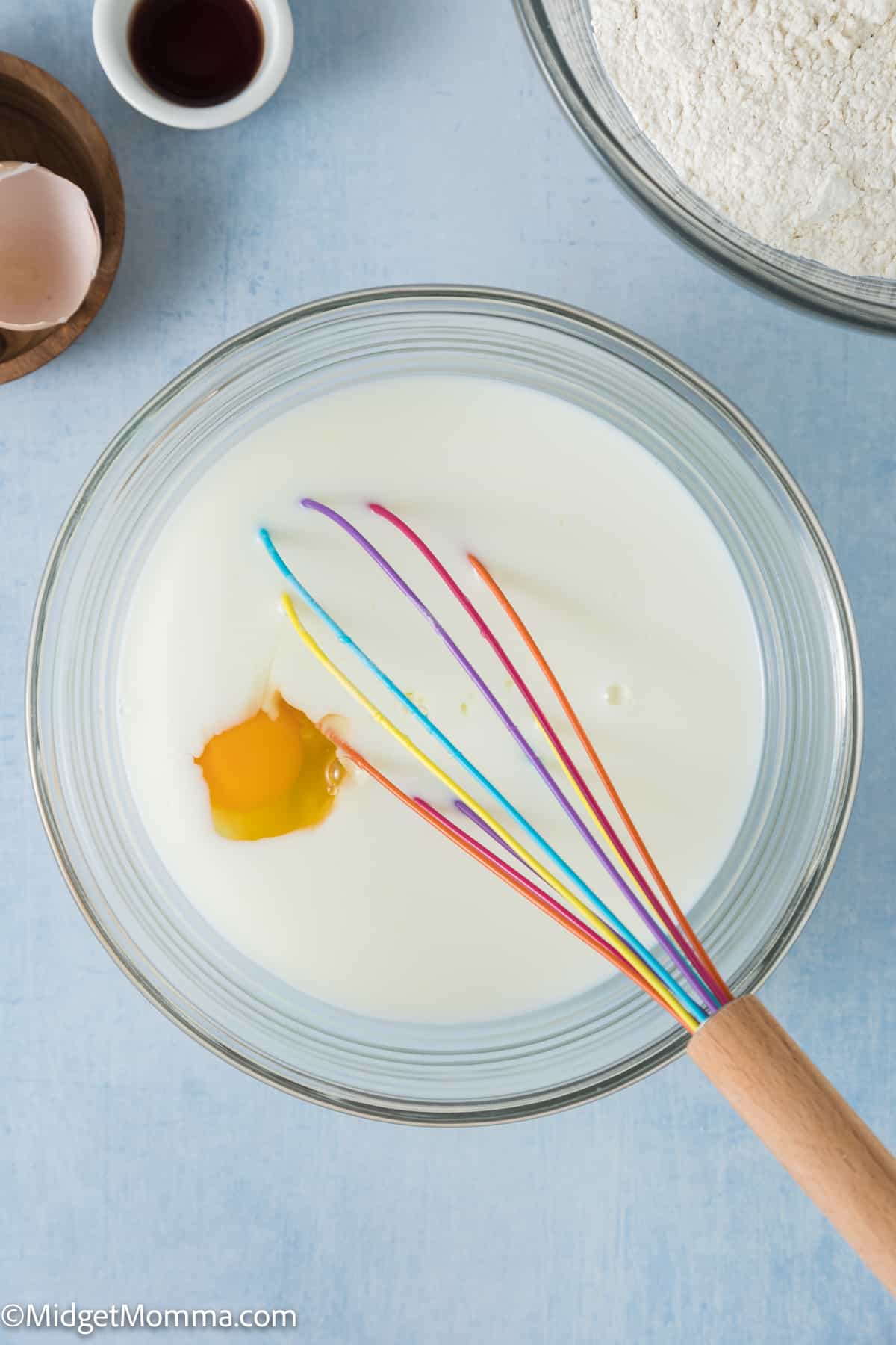 A bowl of milk with a whisk and eggs in it.