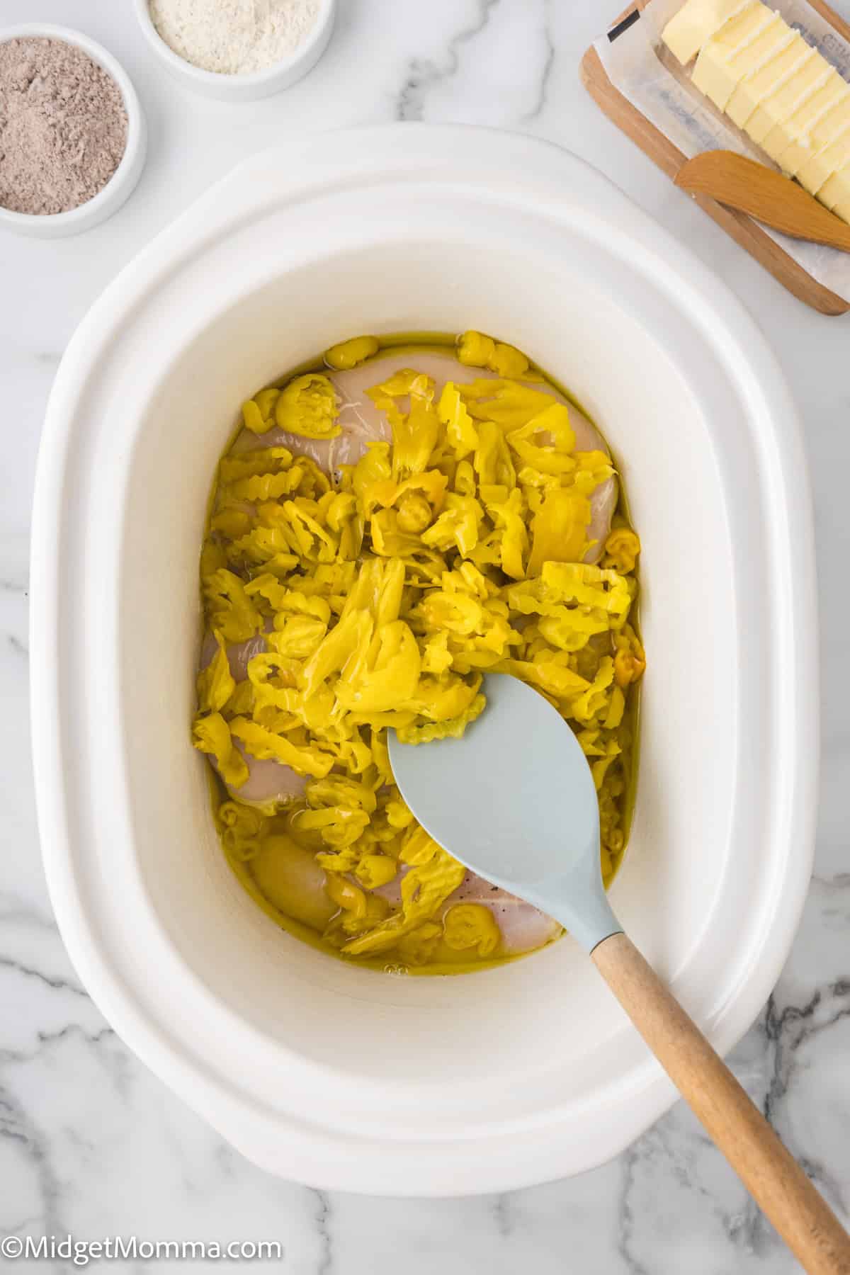 Overhead view of a slow cooker filled with a chicken and peppers with other ingredients like butter are visible on the side.