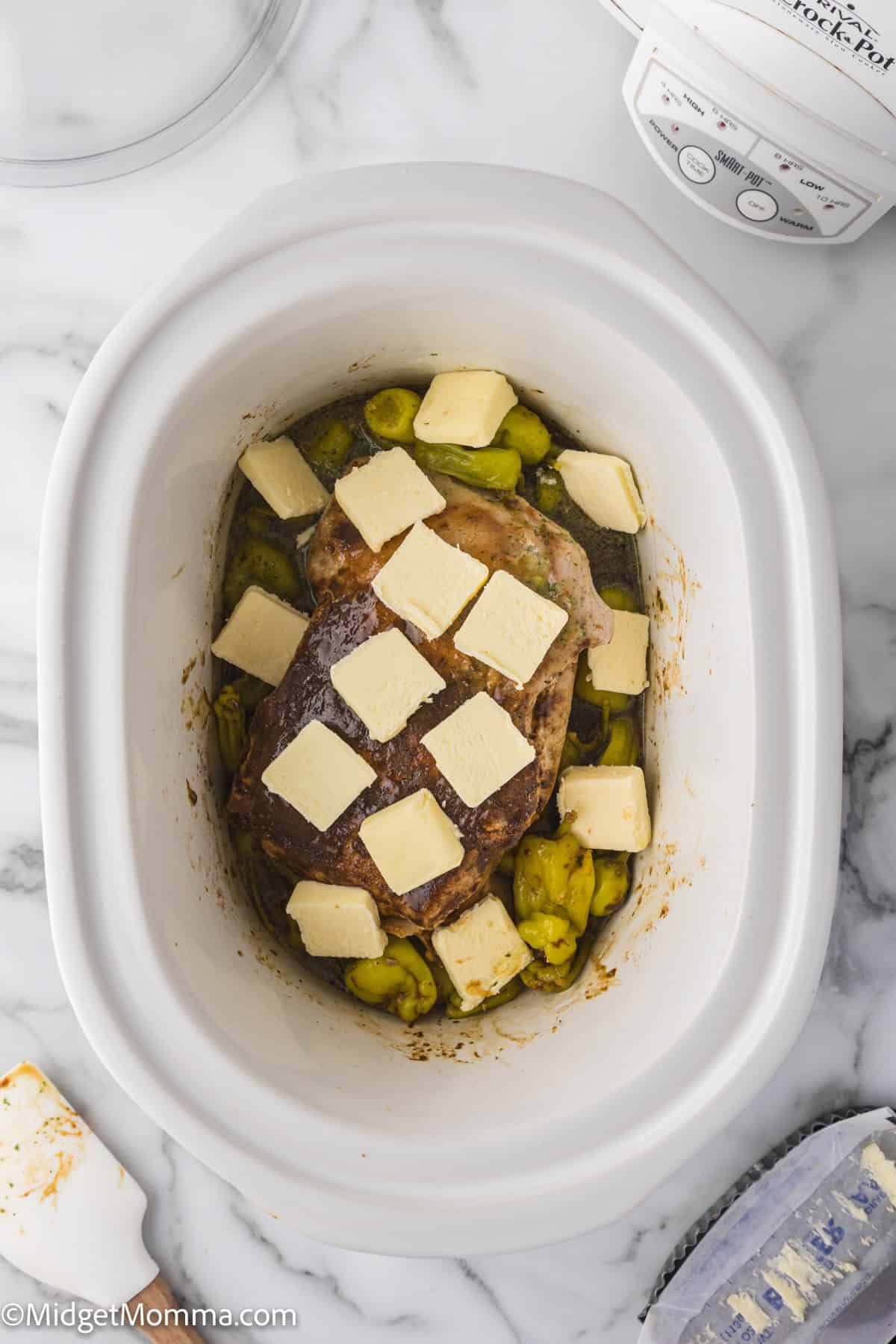 pork roast in a slow cooker topped with dry ranch mix, au jus mix and peppers and chunks of butter.