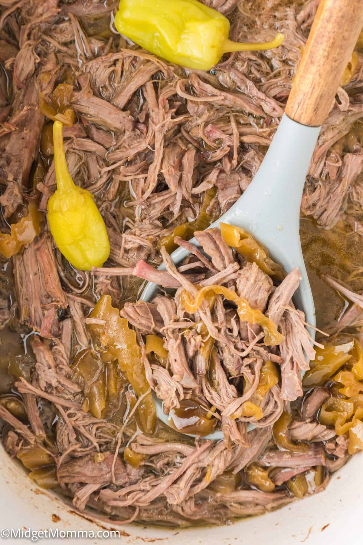 Close-up of a spoon scooping shredded beef and pepperoncini peppers from a dish.