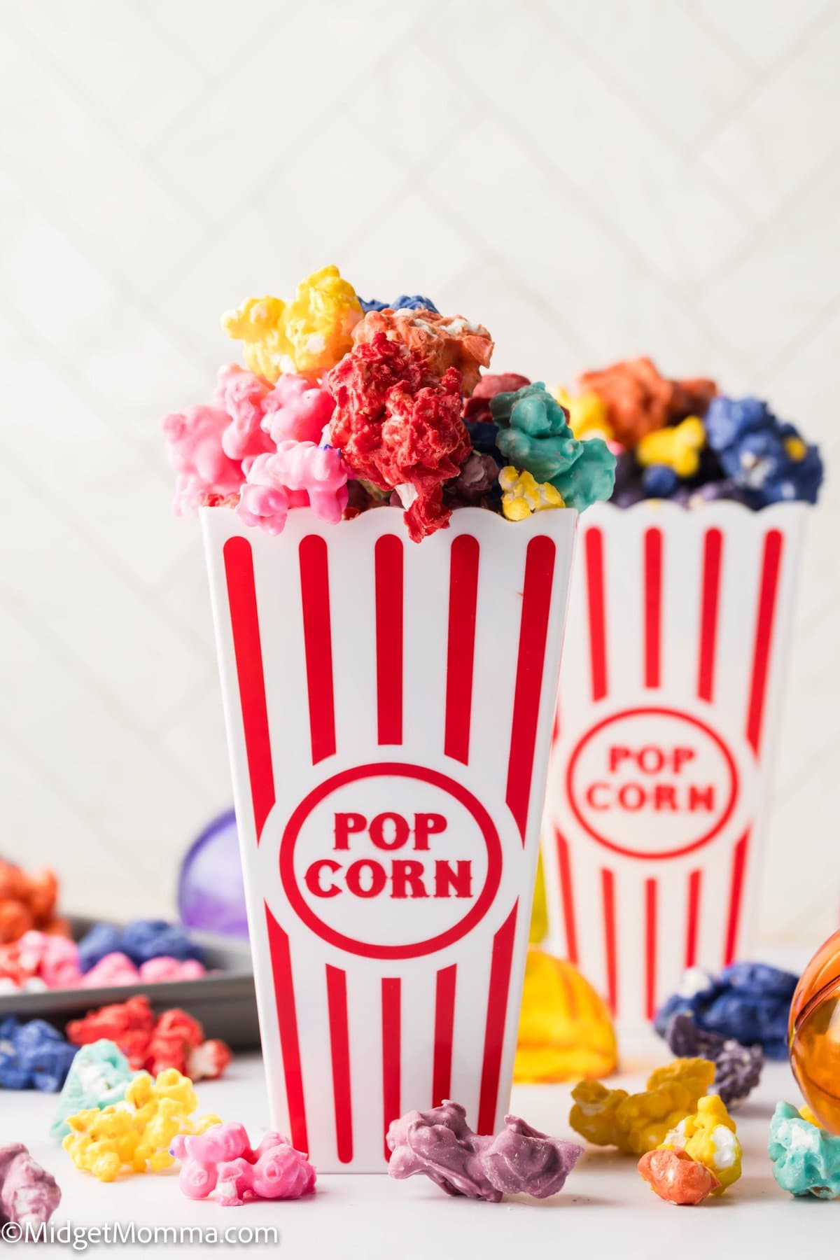 Two red and white striped popcorn containers filled with brightly colored popcorn, with more popcorn scattered around on a light surface.