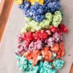Colorful caramel popcorn arranged in rows by color: yellow, blue, green, red, purple, orange, and teal on parchment paper.