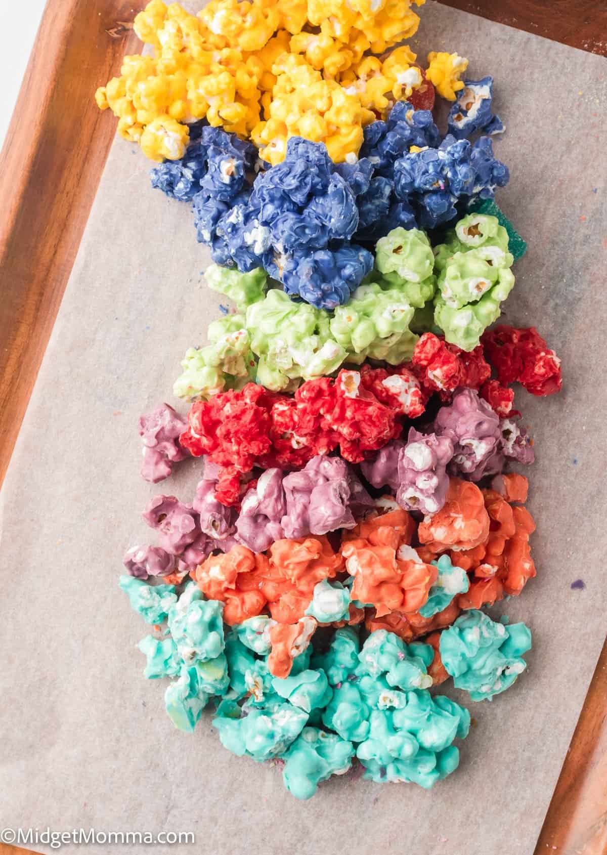 Colorful caramel popcorn arranged in rows by color: yellow, blue, green, red, purple, orange, and teal on parchment paper.