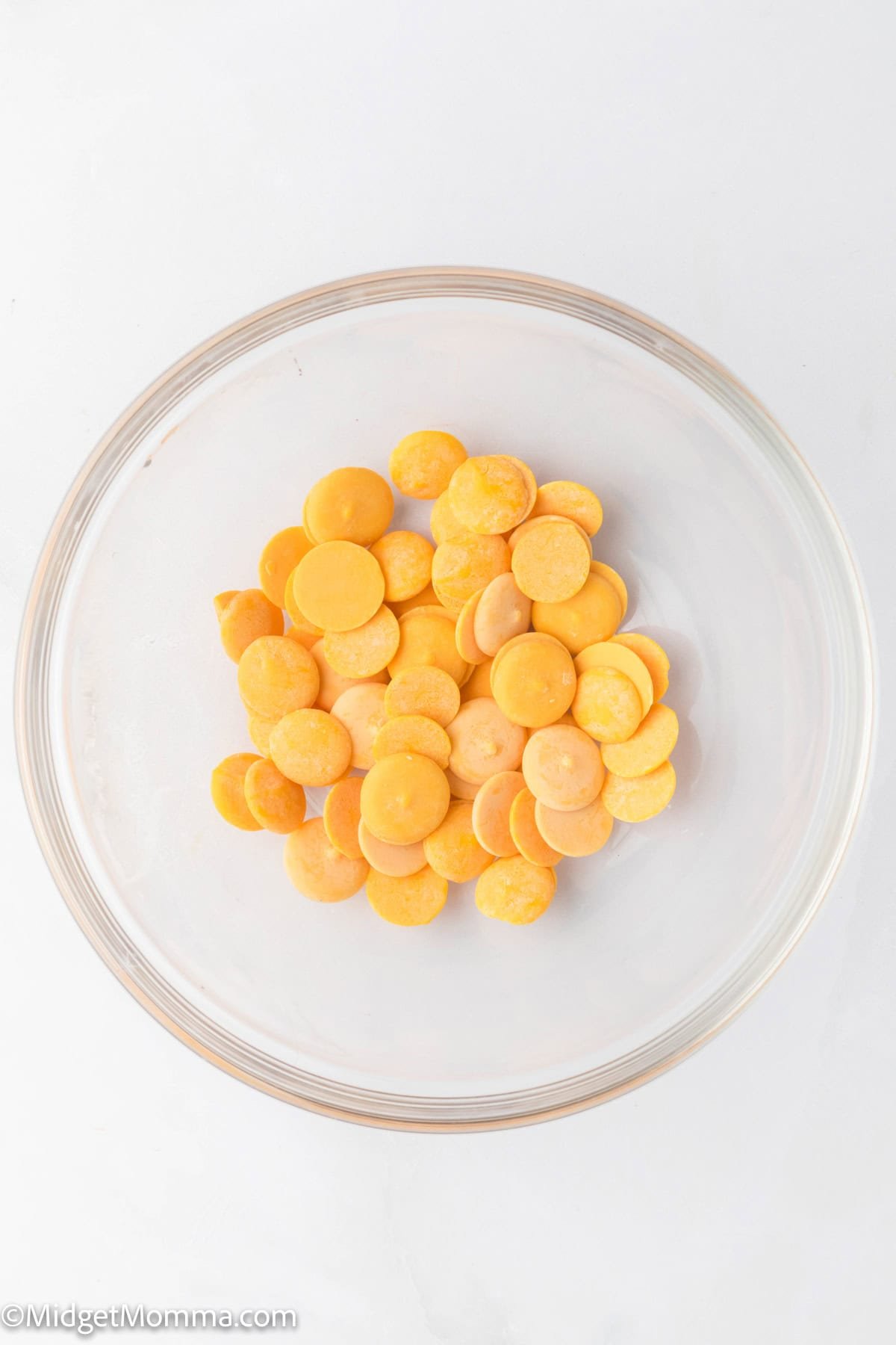 A clear glass bowl containing orange candy melts on a white background.