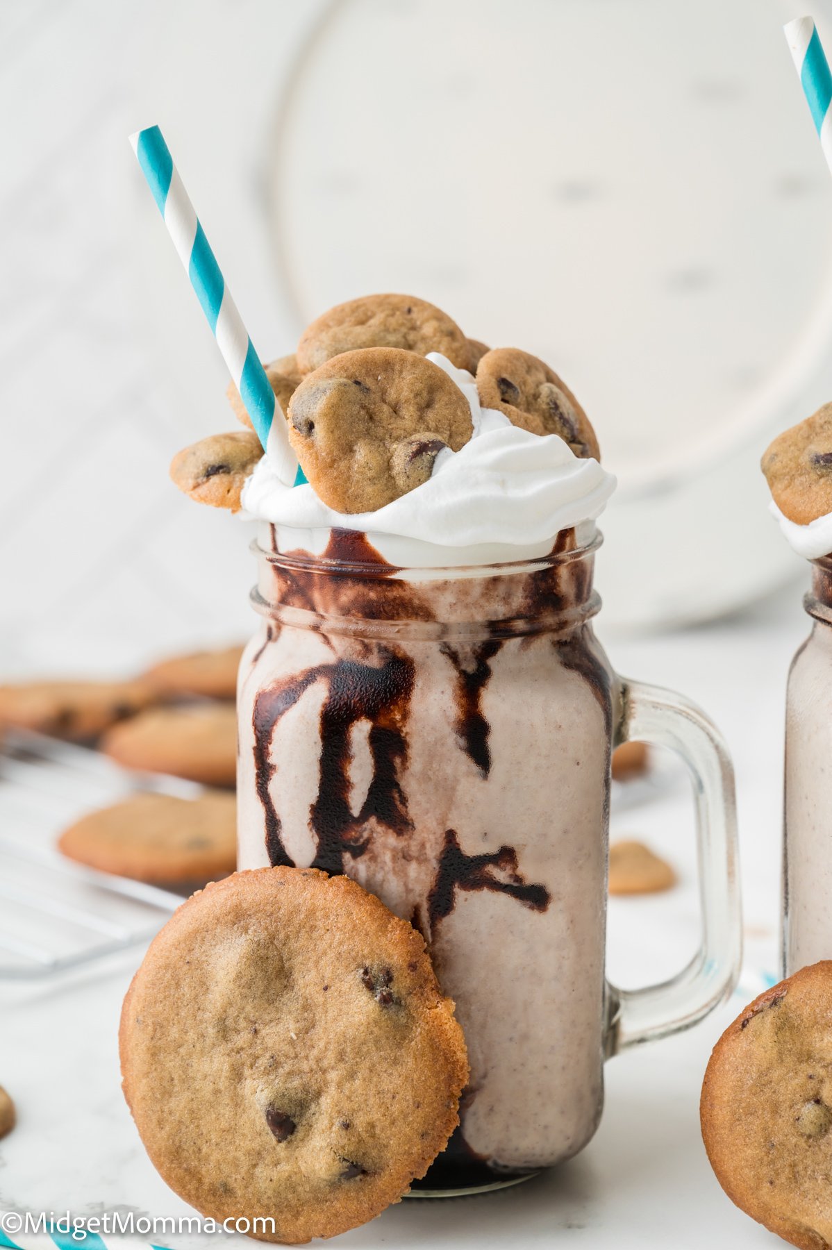 A mason jar filled with a chocolate chip cookie milkshake, topped with whipped cream, chocolate syrup, mini cookies, a blue-striped straw, and a large cookie on the rim.