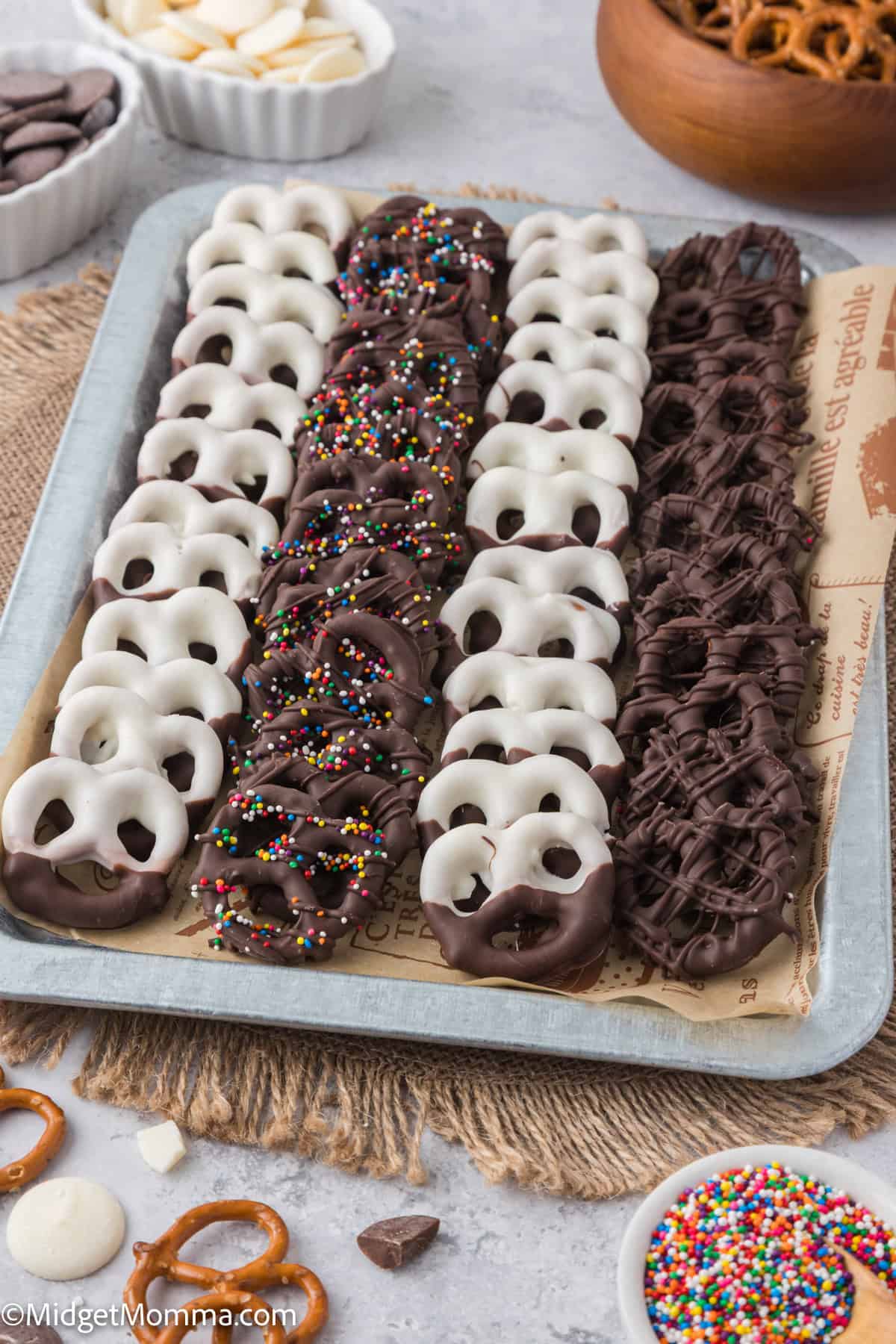 Tray of chocolate-covered pretzels arranged in rows with various toppings, including white chocolate, sprinkles, and dark chocolate drizzle.