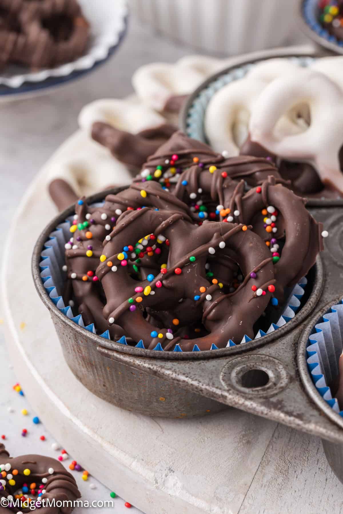 Chocolate-covered pretzels with colorful sprinkles in a muffin tin.