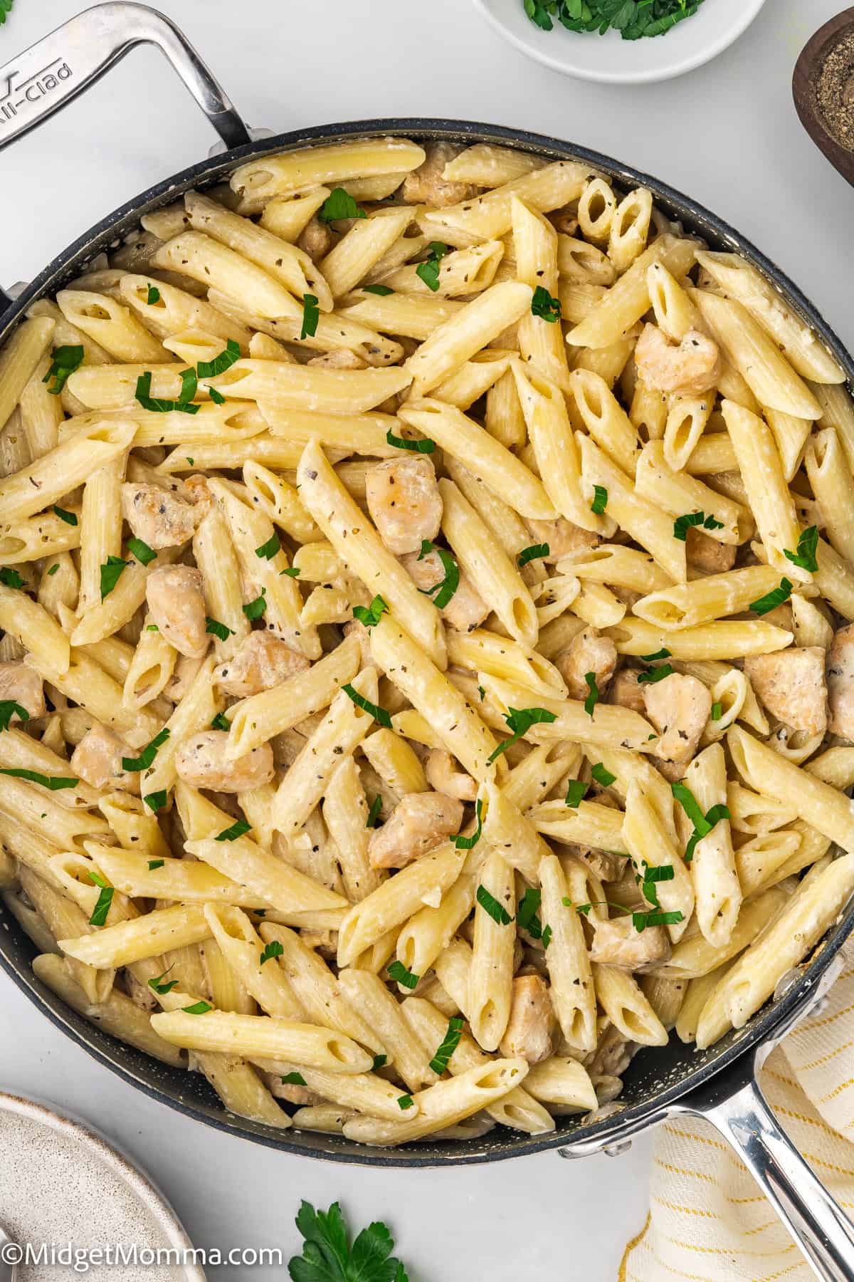 A skillet filled with creamy penne pasta and chicken pieces, garnished with chopped parsley.