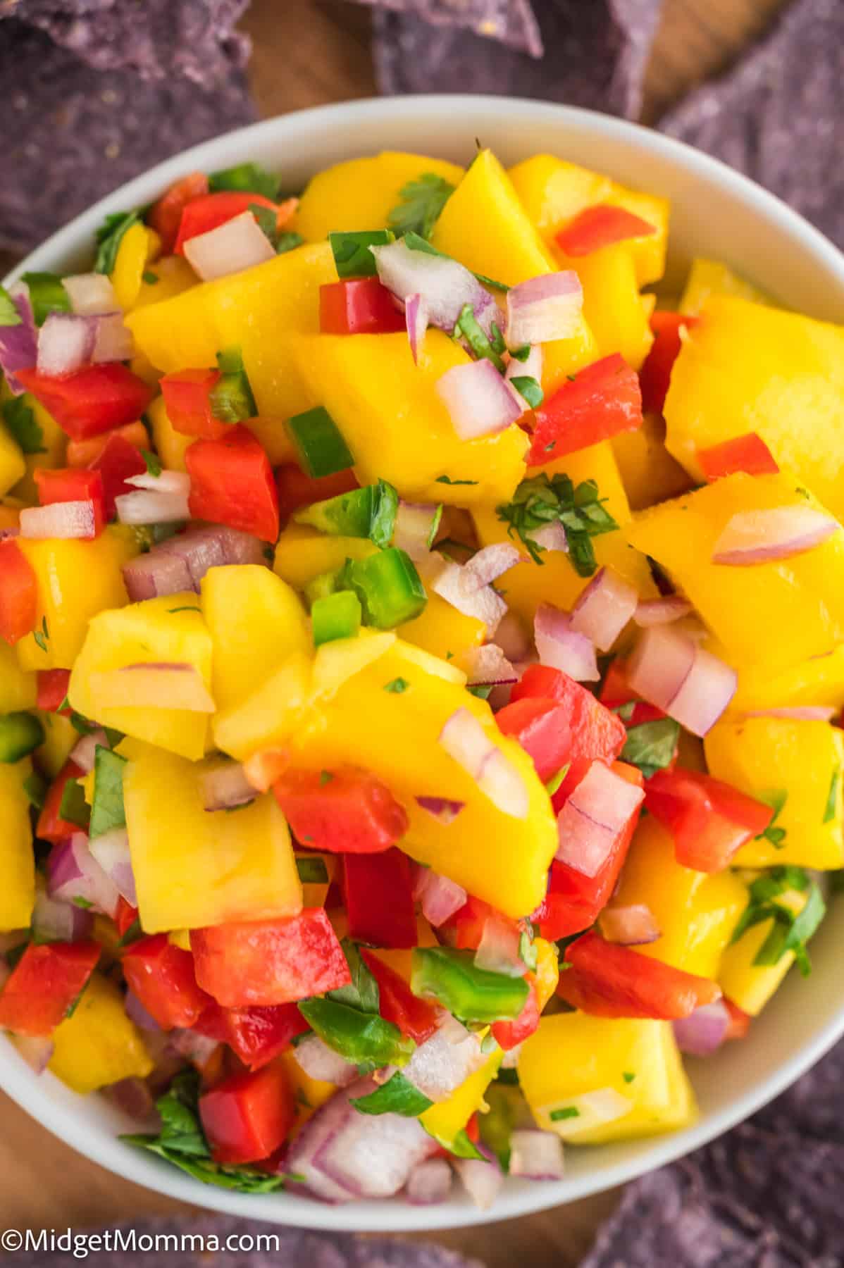 A bowl of mango salsa containing diced mango, red onion, red bell pepper, cilantro, and jalapeño, surrounded by tortilla chips.