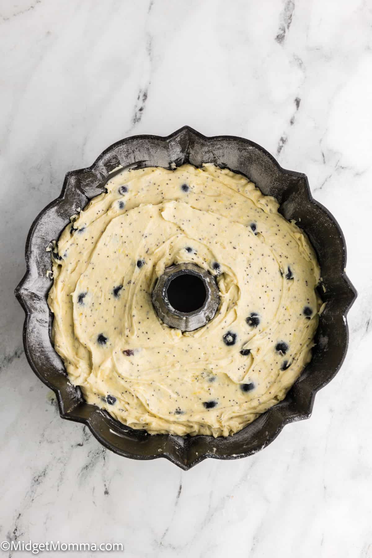 Bundt pan filled with blueberry cake batter on a marble surface.