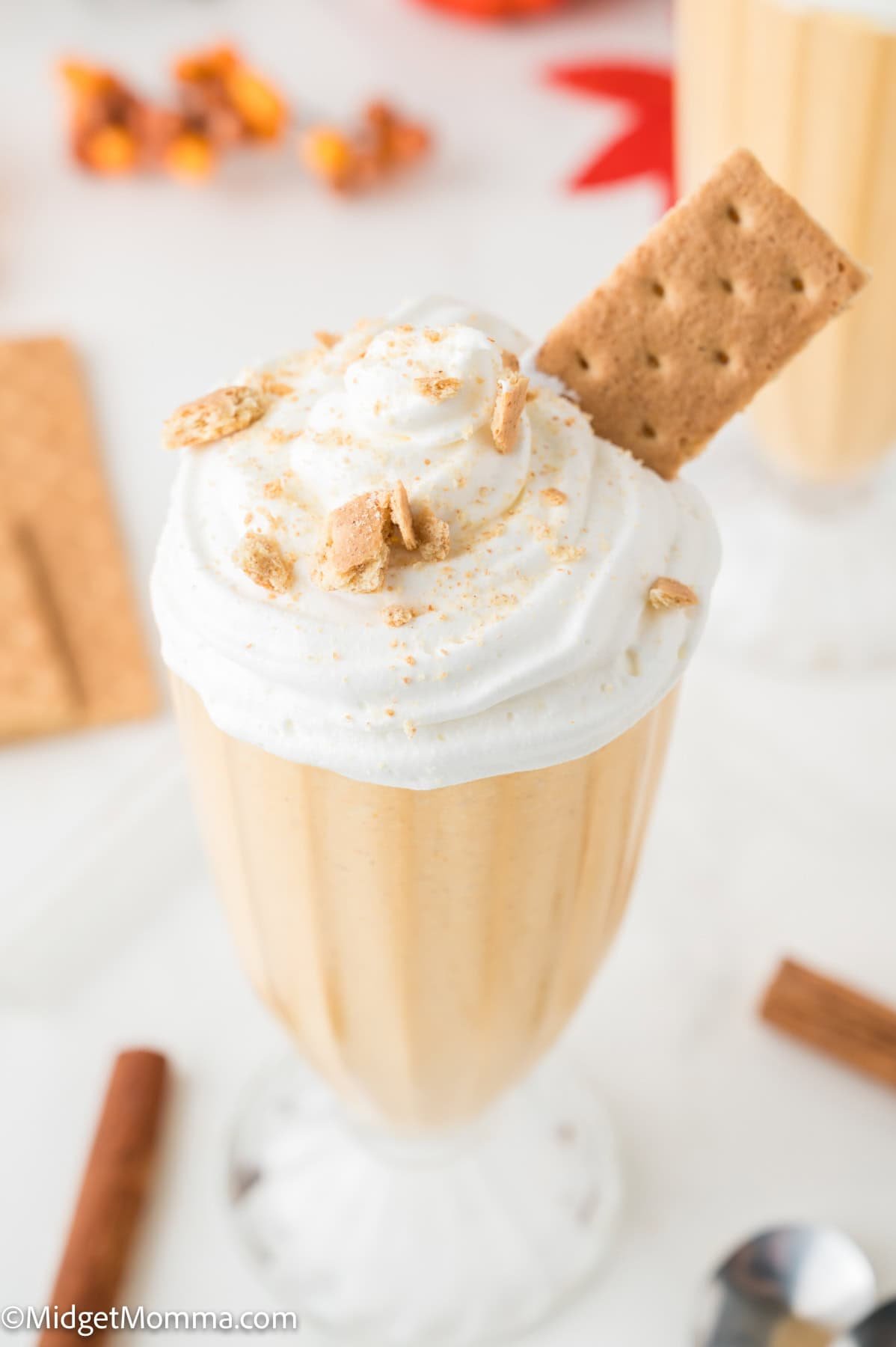 A glass of creamy pumpkin milkshake topped with whipped cream, crushed graham crackers, and a whole graham cracker stick.