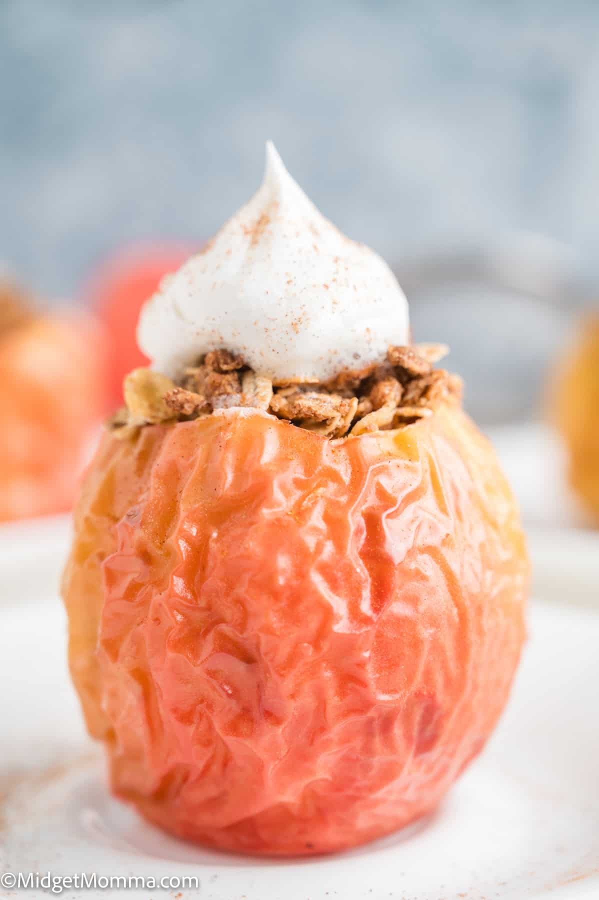A baked apple filled with granola and topped with a swirl of whipped cream sits on a white plate.
