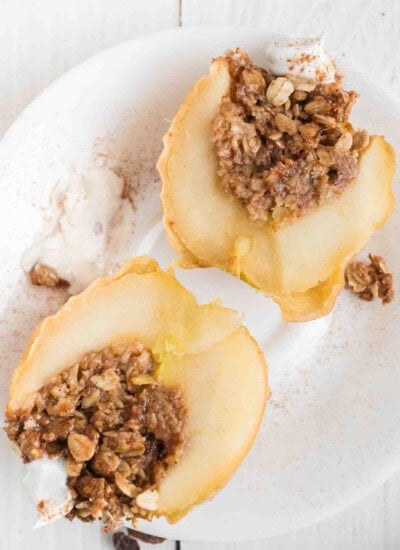 Two baked apple halves on a white plate, each filled with an oat and nut crumble, served with a scoop of vanilla ice cream.