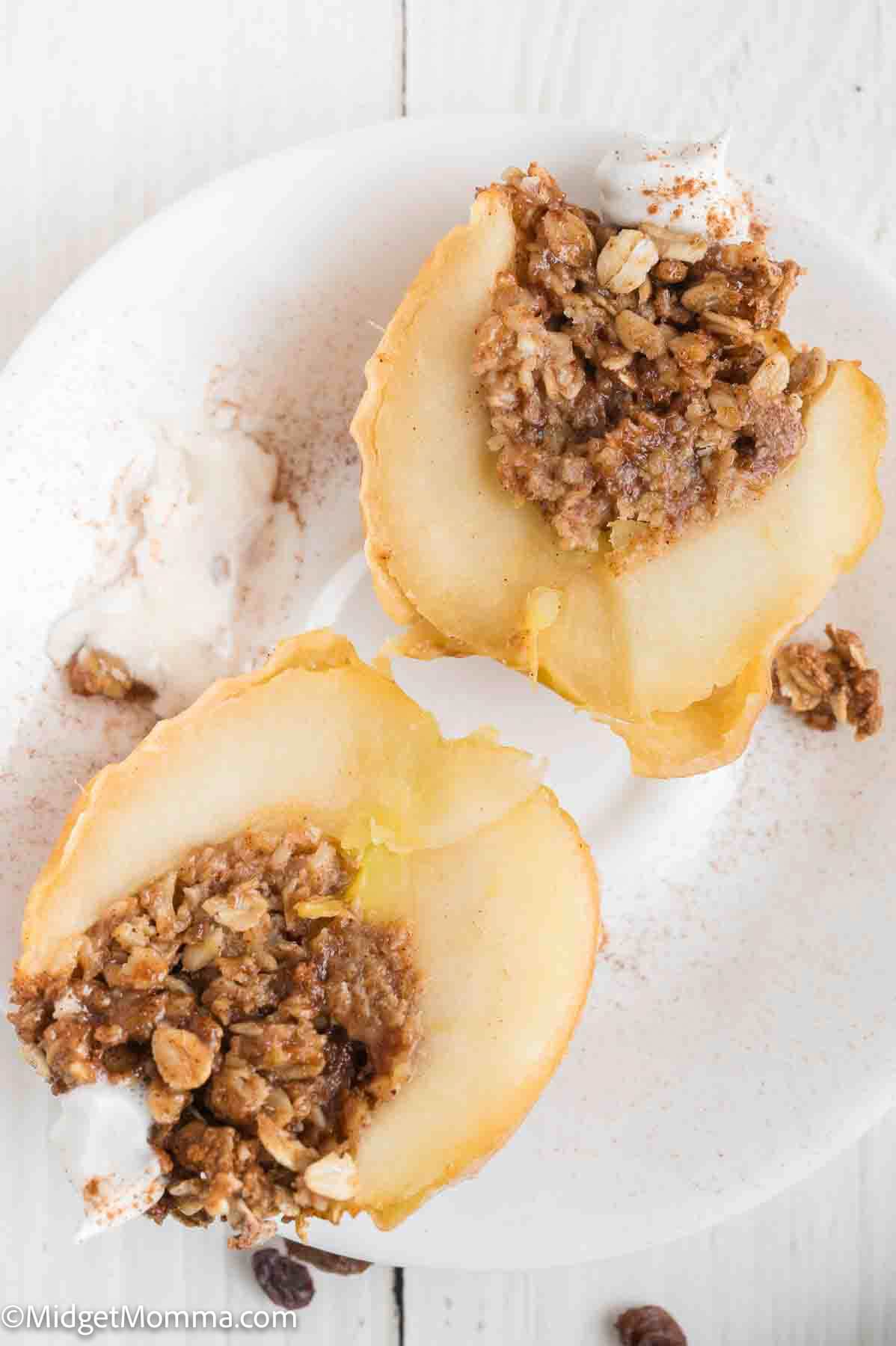 Two baked apple halves on a white plate, each filled with an oat and nut crumble, served with a scoop of vanilla ice cream.