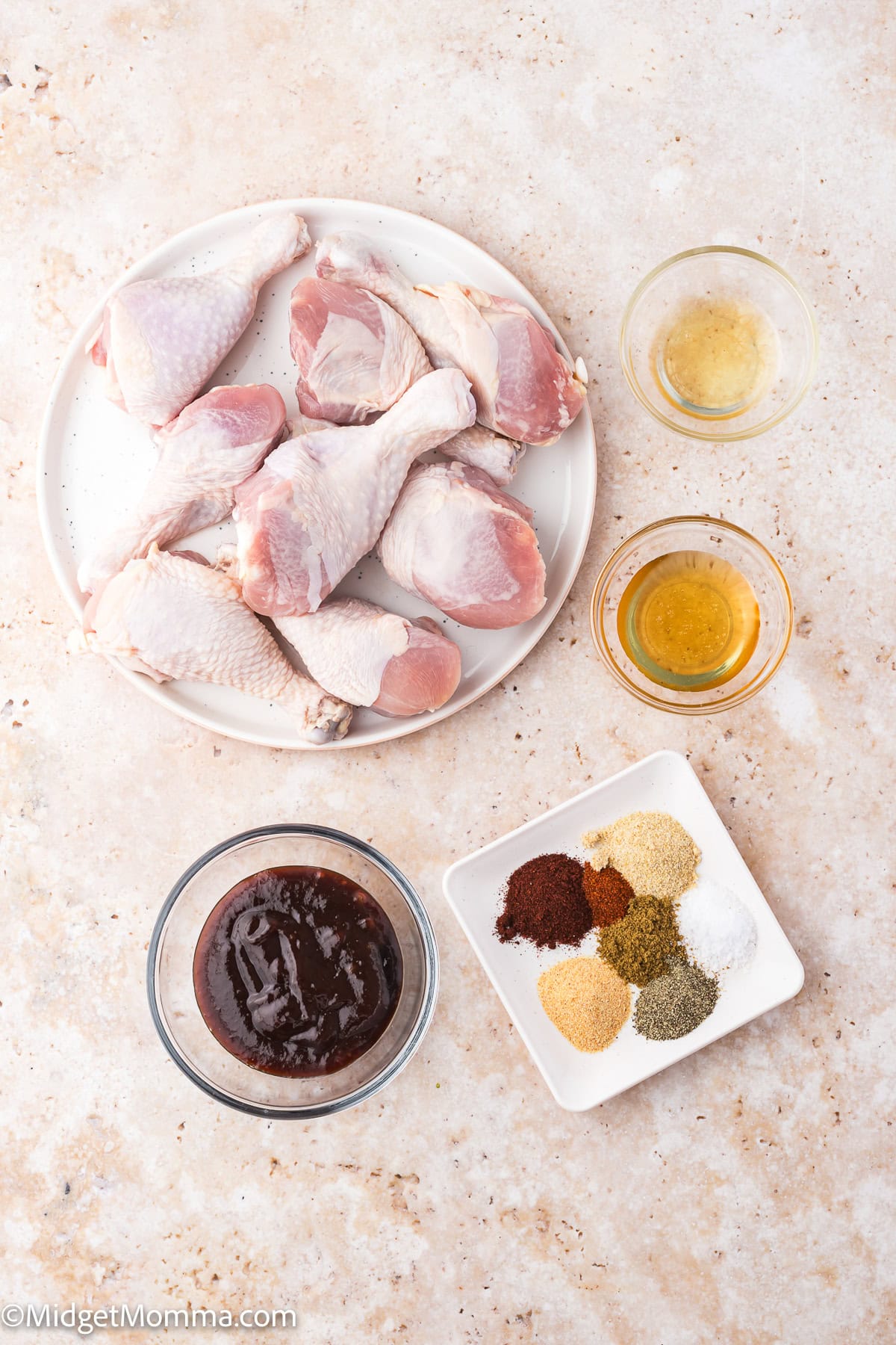 Raw chicken drumsticks on a plate, with small bowls of sauce, oil, and apple cider vinegar, and a dish of various ground spices arranged on a light surface.