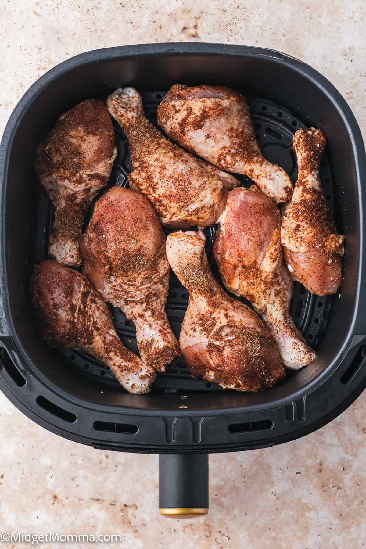 Raw, seasoned chicken drumsticks arranged in a single layer inside an air fryer basket, ready to be cooked.
