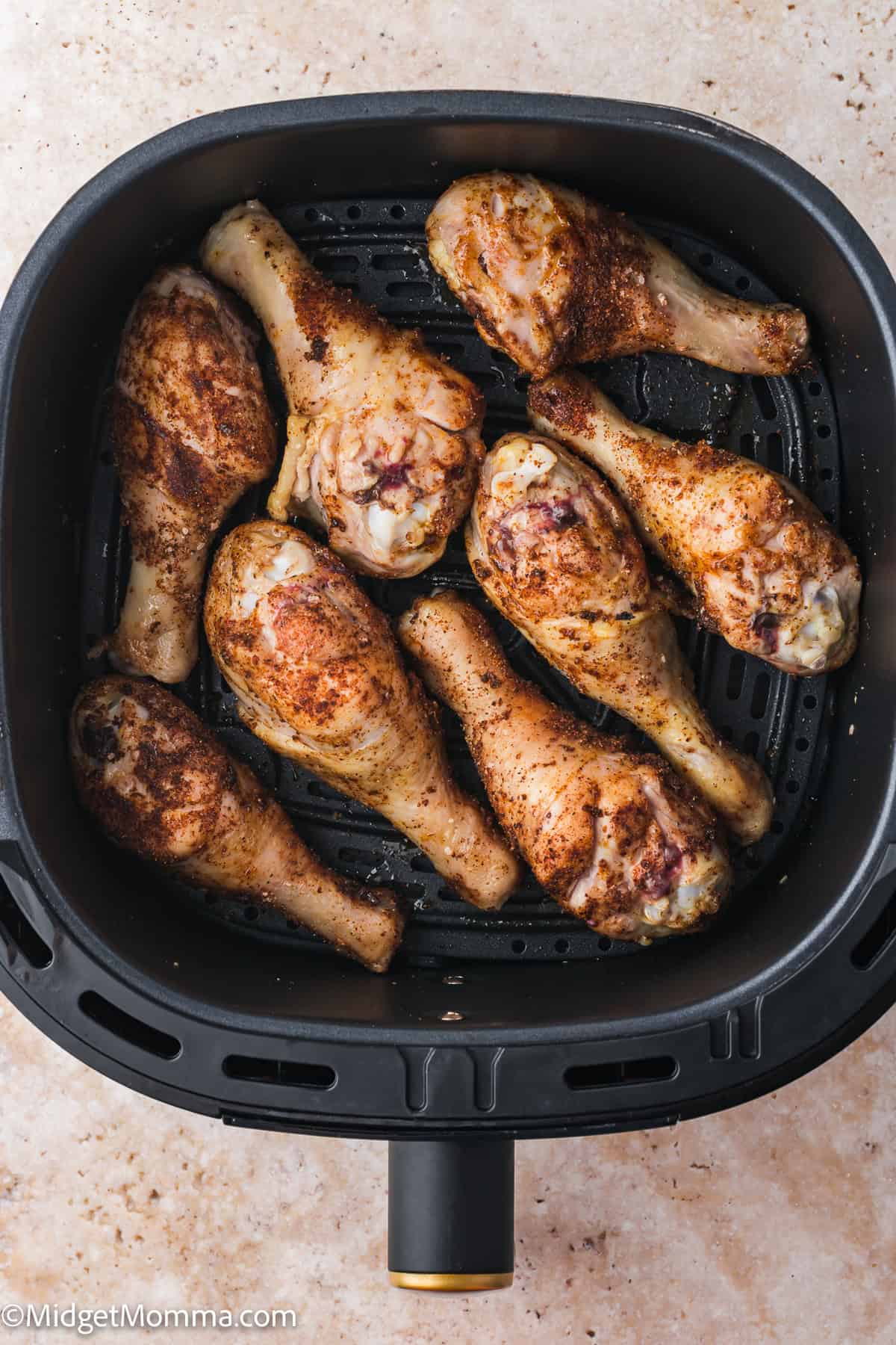 Seven seasoned chicken drumsticks arranged in a single layer inside an air fryer basket, ready to be cooked.
