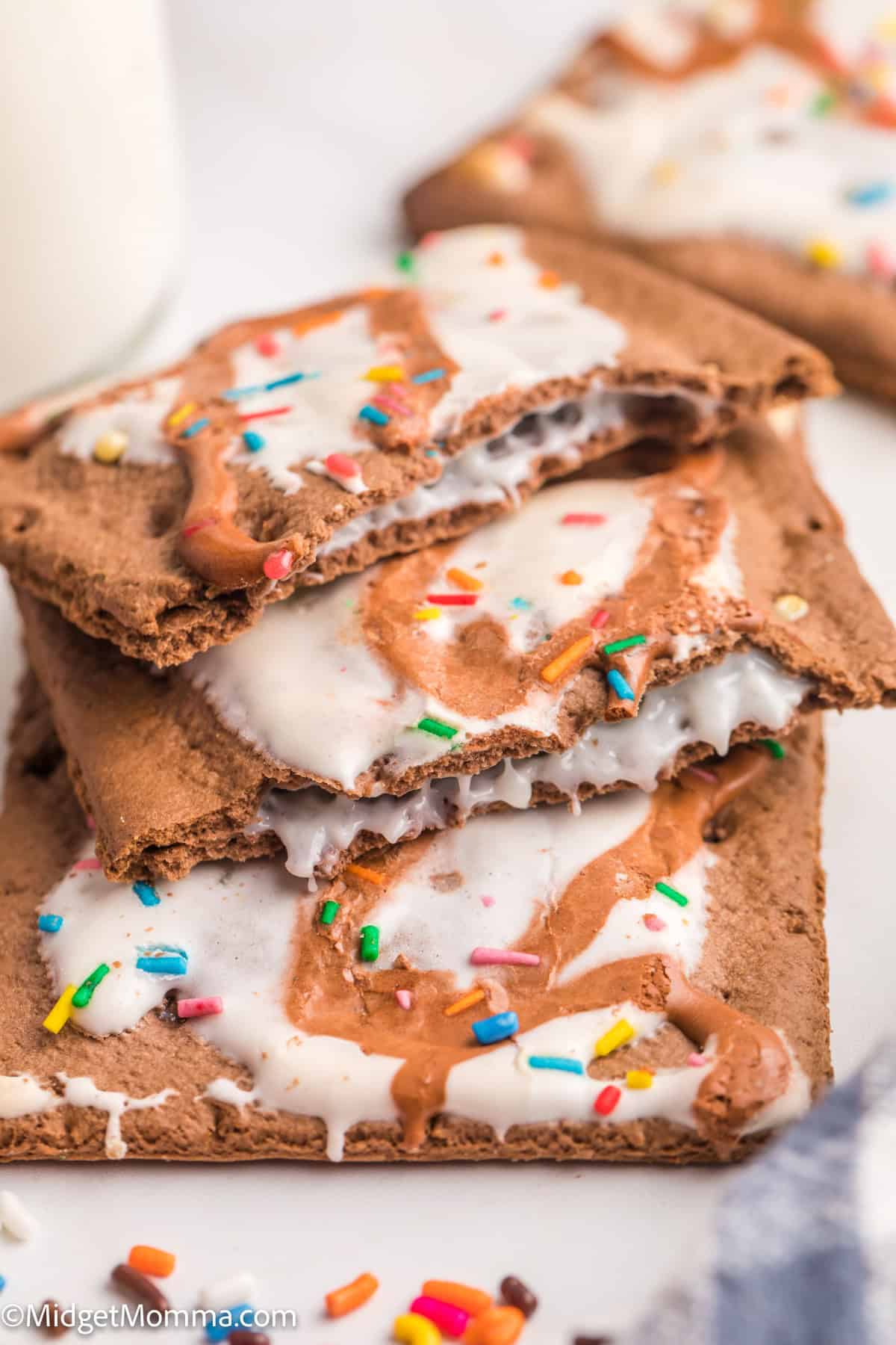 Three frosted chocolate toaster pastries with white icing and colorful sprinkles are stacked on a white surface.