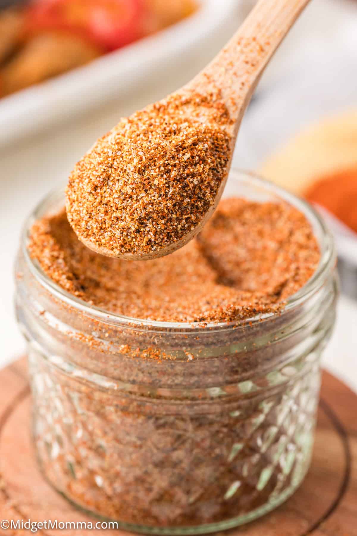 A wooden spoon holds taco seasoning above a small glass jar filled with more of the spice blend.
