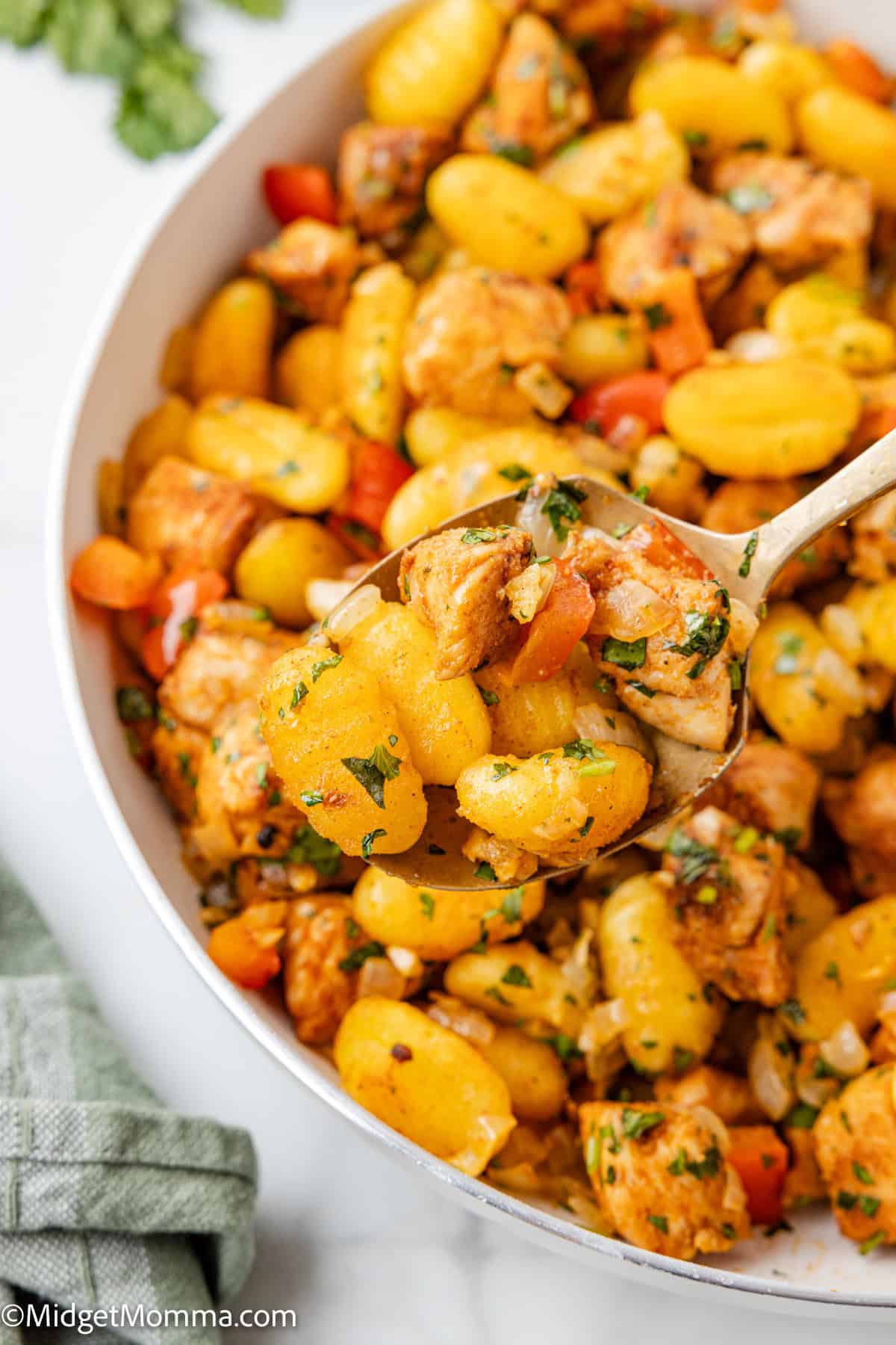 A close-up of a skillet with cooked gnocchi, diced chicken, and vegetables being served with a spoon.