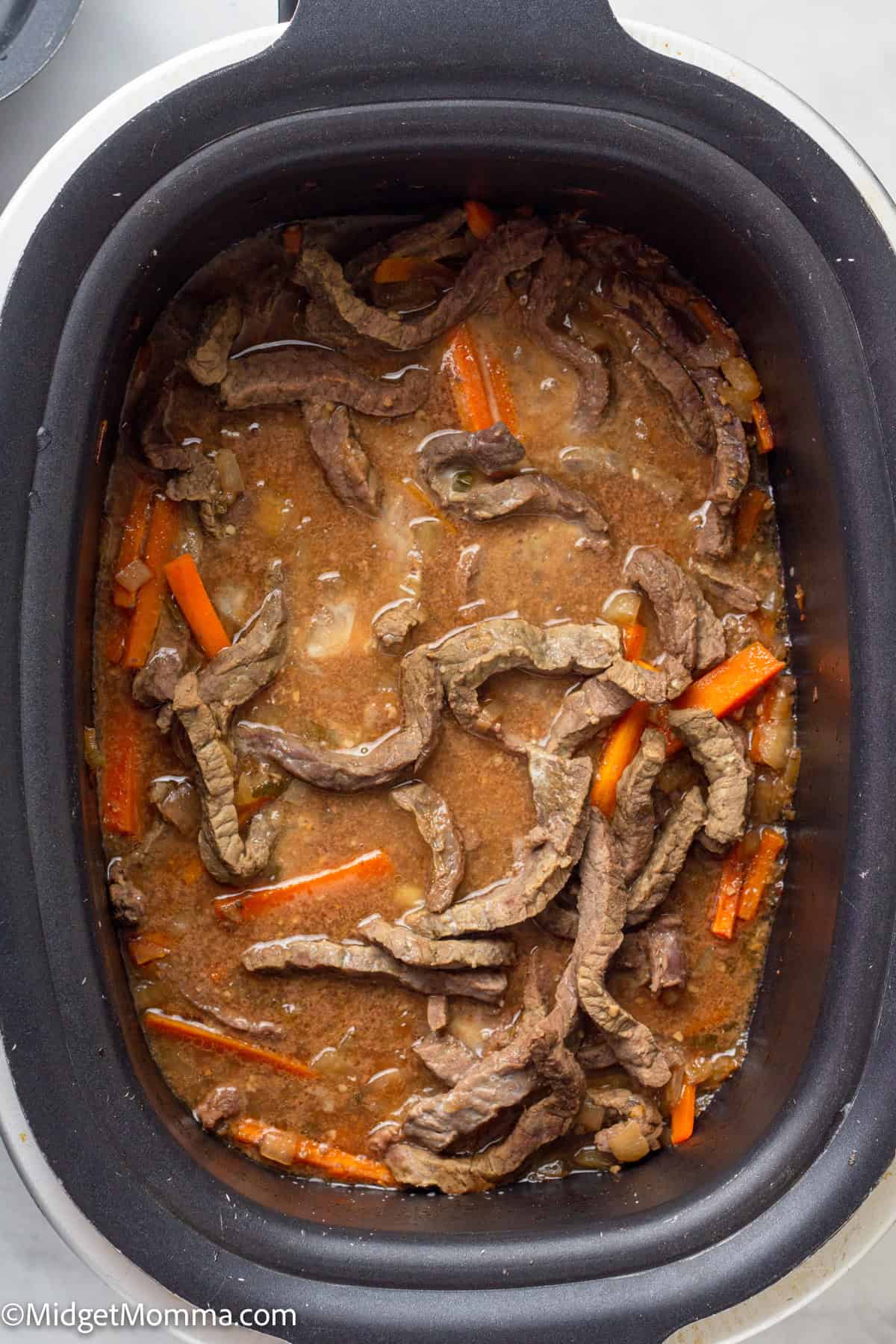 Beef strips and carrot pieces in a brown sauce, cooked in a slow cooker.