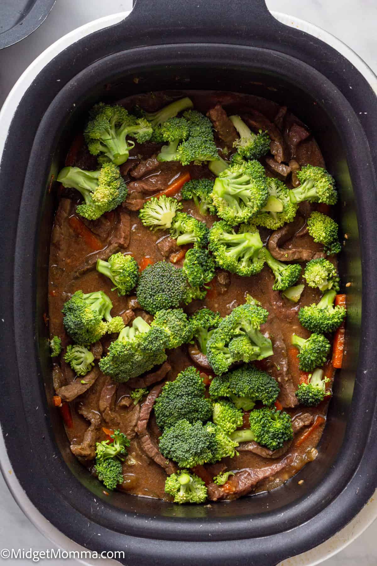 Slices of beef and broccoli florets in a brown sauce, placed inside a slow cooker.