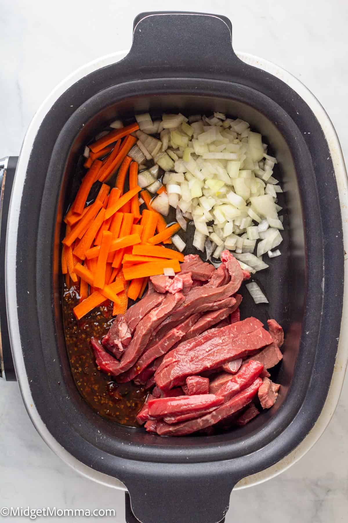 Sliced raw beef, chopped onions, and carrot sticks are arranged in a slow cooker with sauce at the bottom.