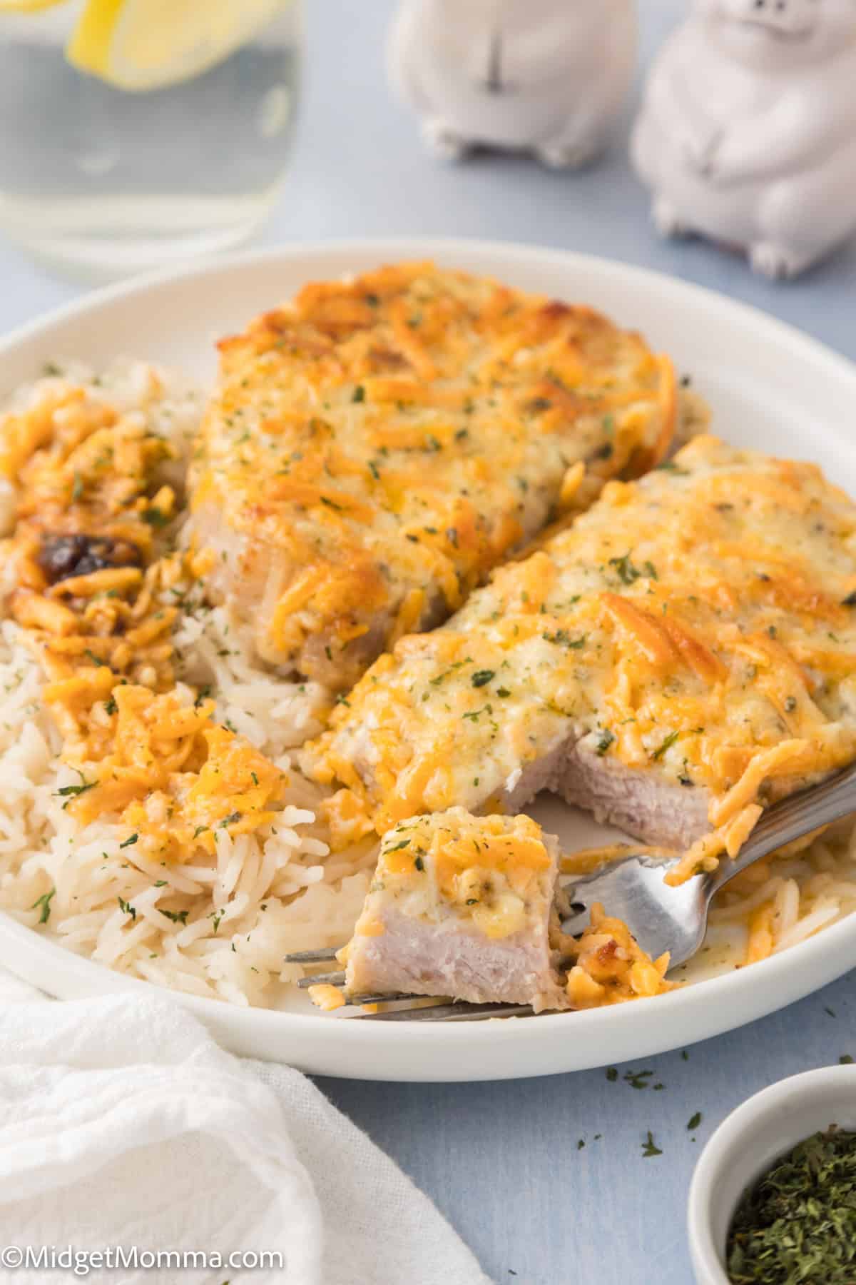A plate of white rice topped with two pieces of baked, cheese-covered chicken, with a fork holding a bite-sized piece.