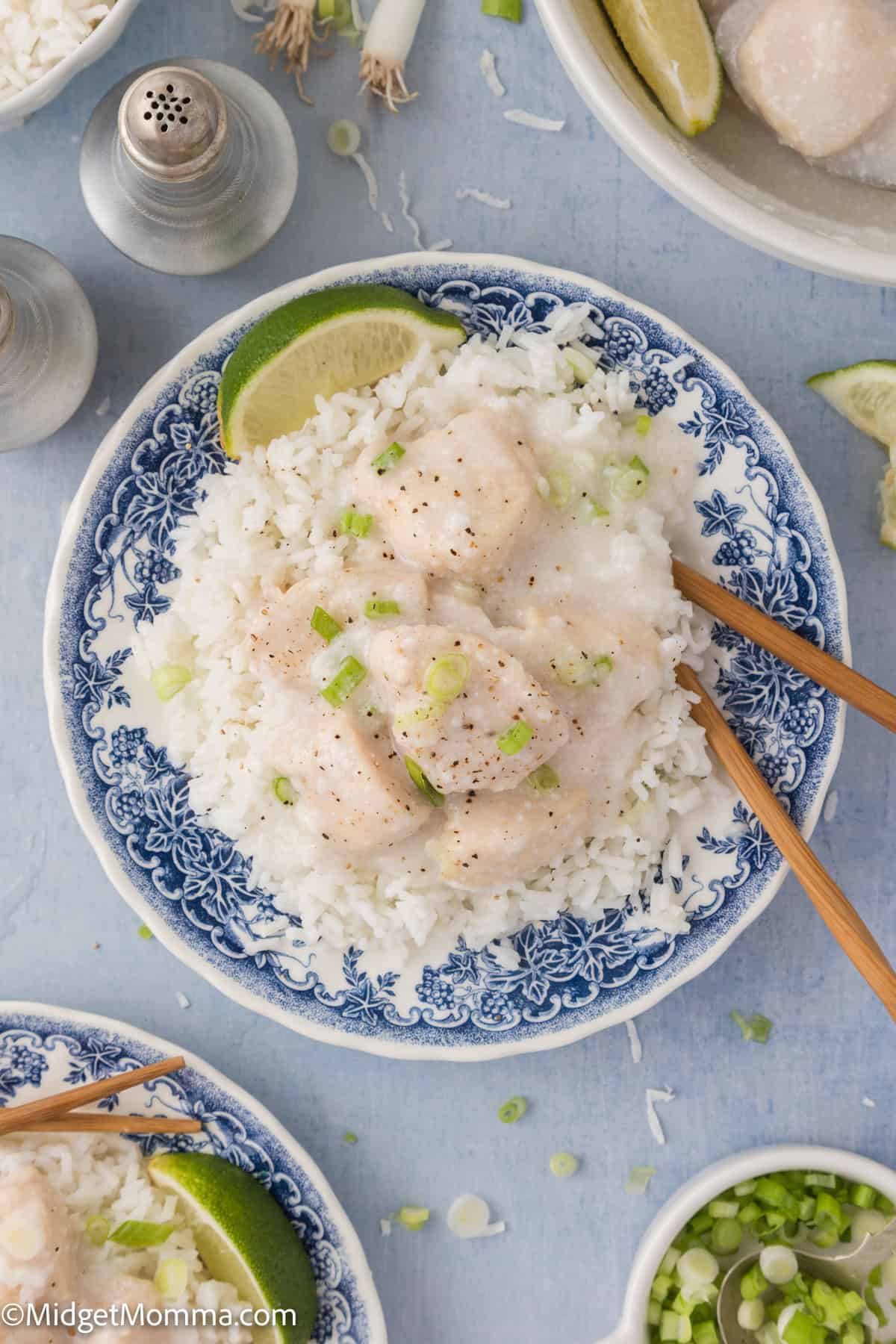 A blue-and-white plate with white rice topped with creamy chicken, garnished with chopped green onions, lime wedge, and chopsticks on the side.