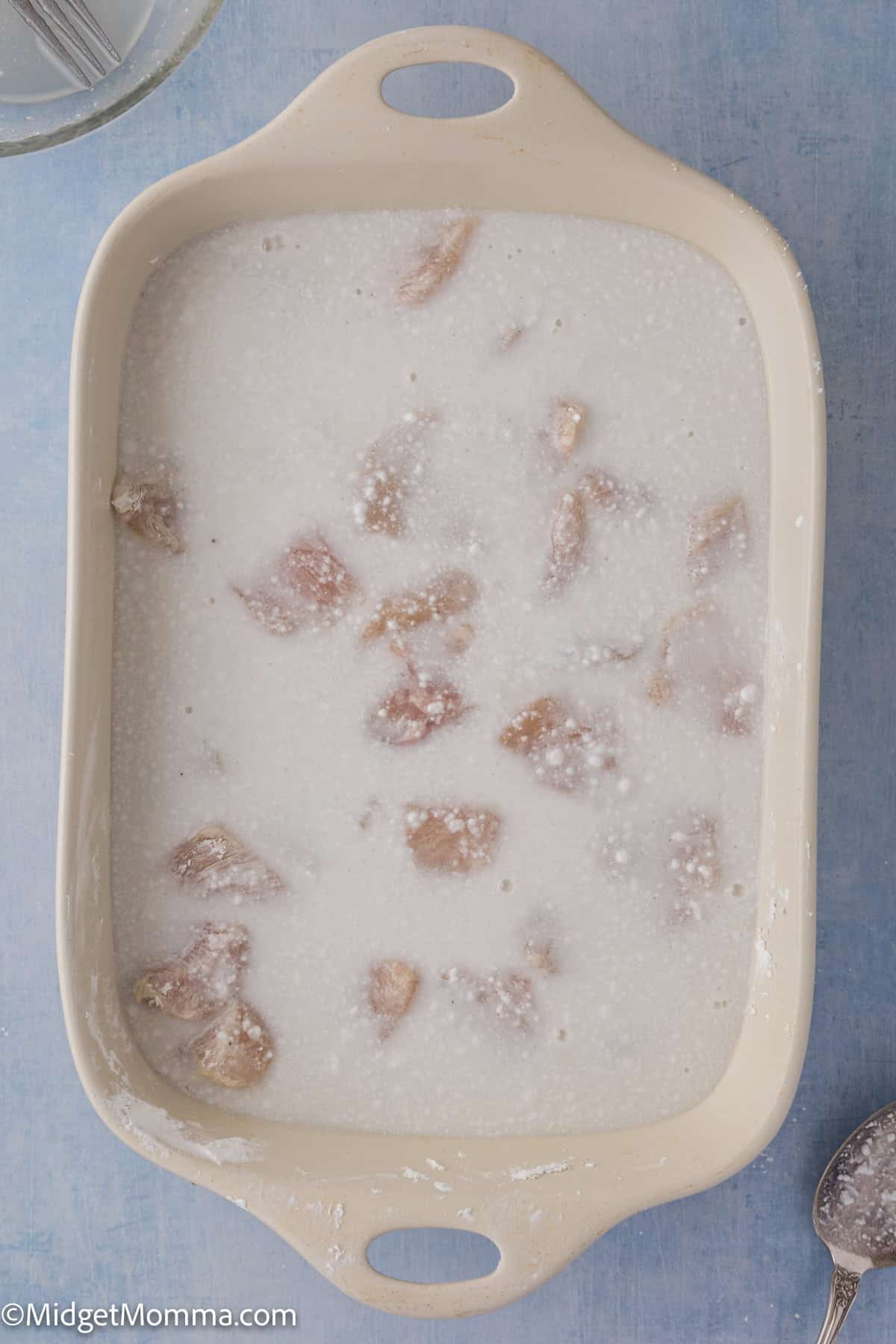 A rectangular baking dish filled with raw chicken pieces covered in coconut milk.