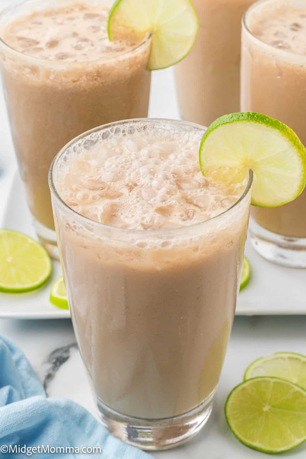 Three glasses of iced creamy beverage garnished with lime slices on the rim, with extra lime slices on the table nearby.