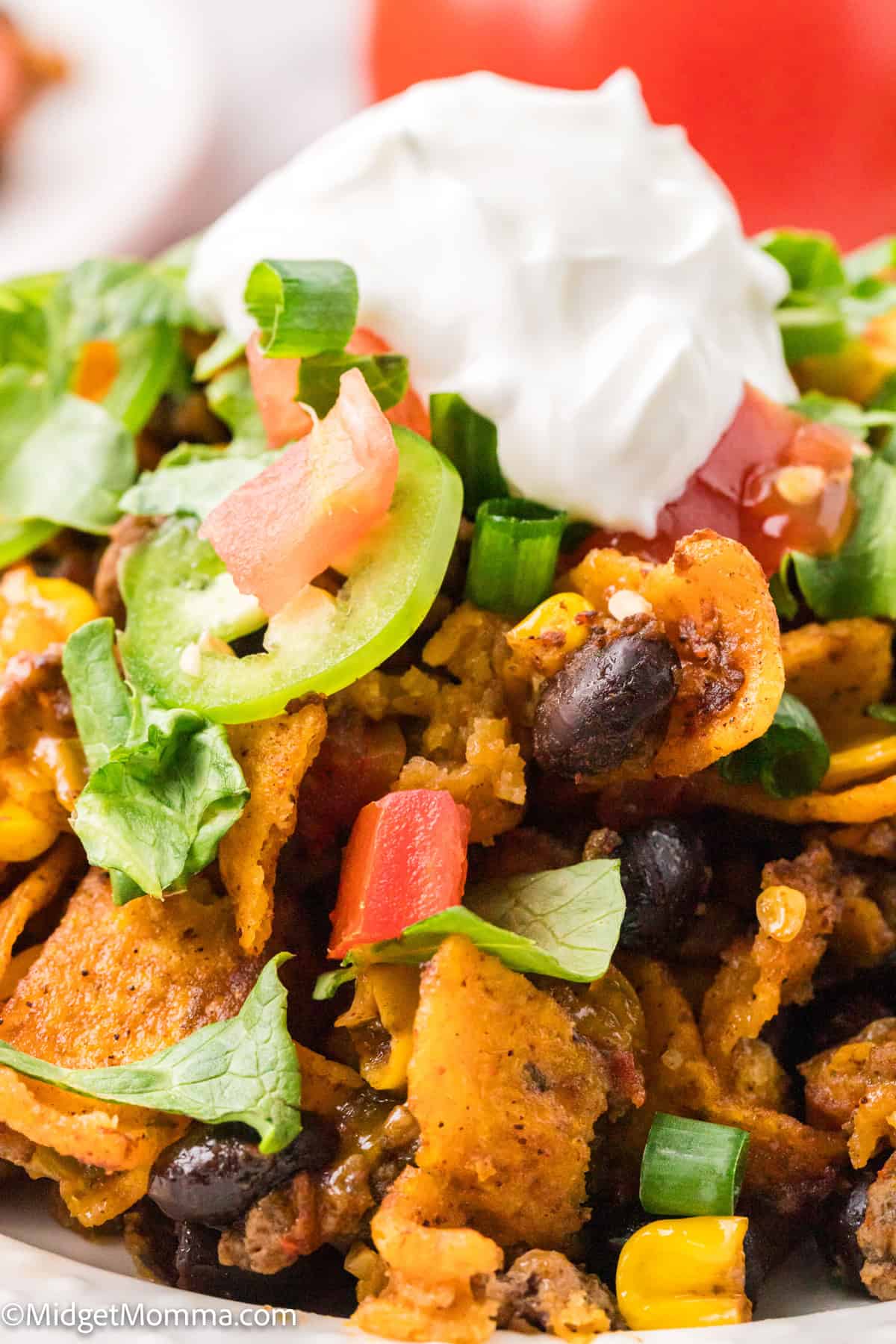 Close-up of a plate of taco salad with corn chips, black beans, corn, diced tomatoes, jalapeño slices, green onions, lettuce, and a dollop of sour cream on top.