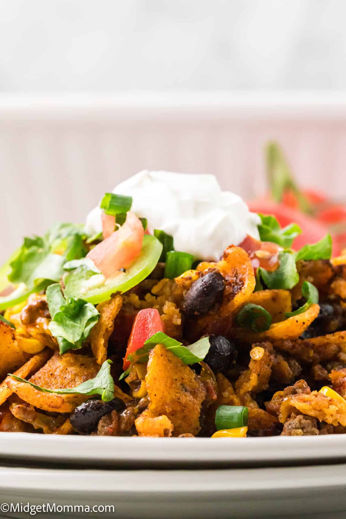 A plate of taco salad topped with corn chips, black beans, lettuce, tomatoes, green onions, and a dollop of sour cream.