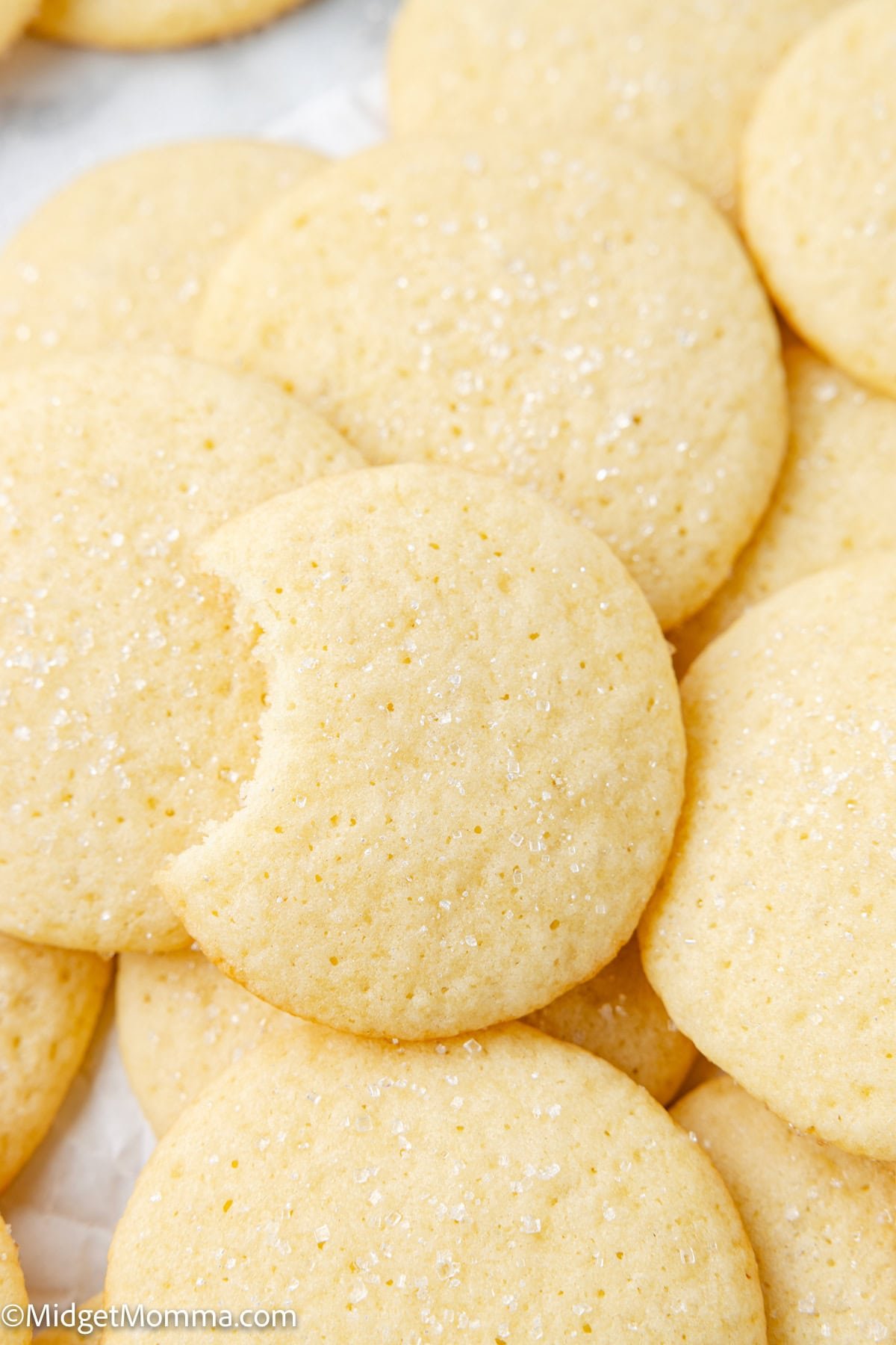 A close-up of several sugar cookies, with one cookie showing a bite taken out of it. The cookies are lightly sprinkled with sugar.
