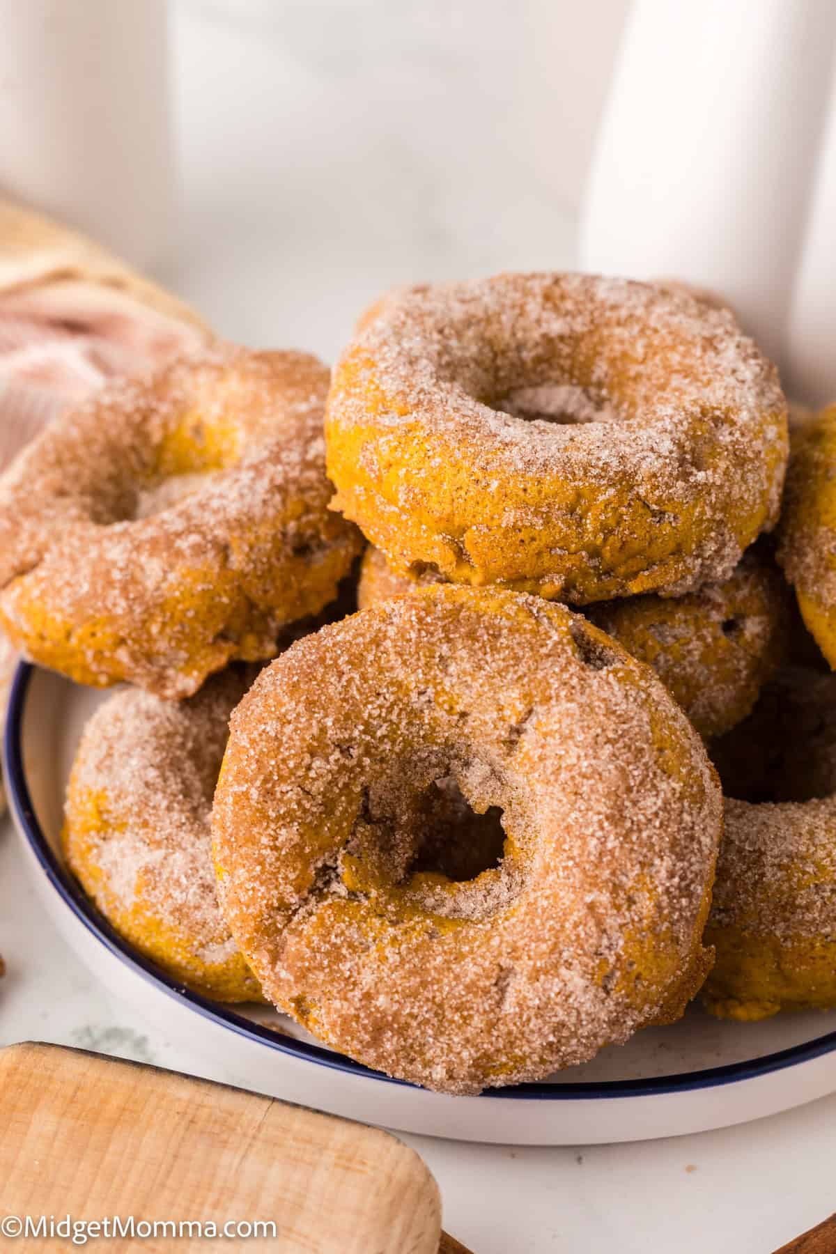 A plate stacked with several sugar-coated donuts, displayed on a white surface.