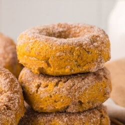 Baked pumpkin donuts. A stack of three baked donuts covered in cinnamon sugar, with another donut partially visible on the left.