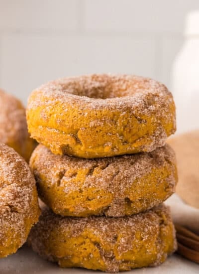 Baked pumpkin donuts. A stack of three baked donuts covered in cinnamon sugar, with another donut partially visible on the left.