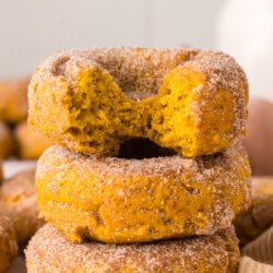 Three cinnamon sugar-coated donuts are stacked on top of each other, with the top donut showing a large bite taken out of it.