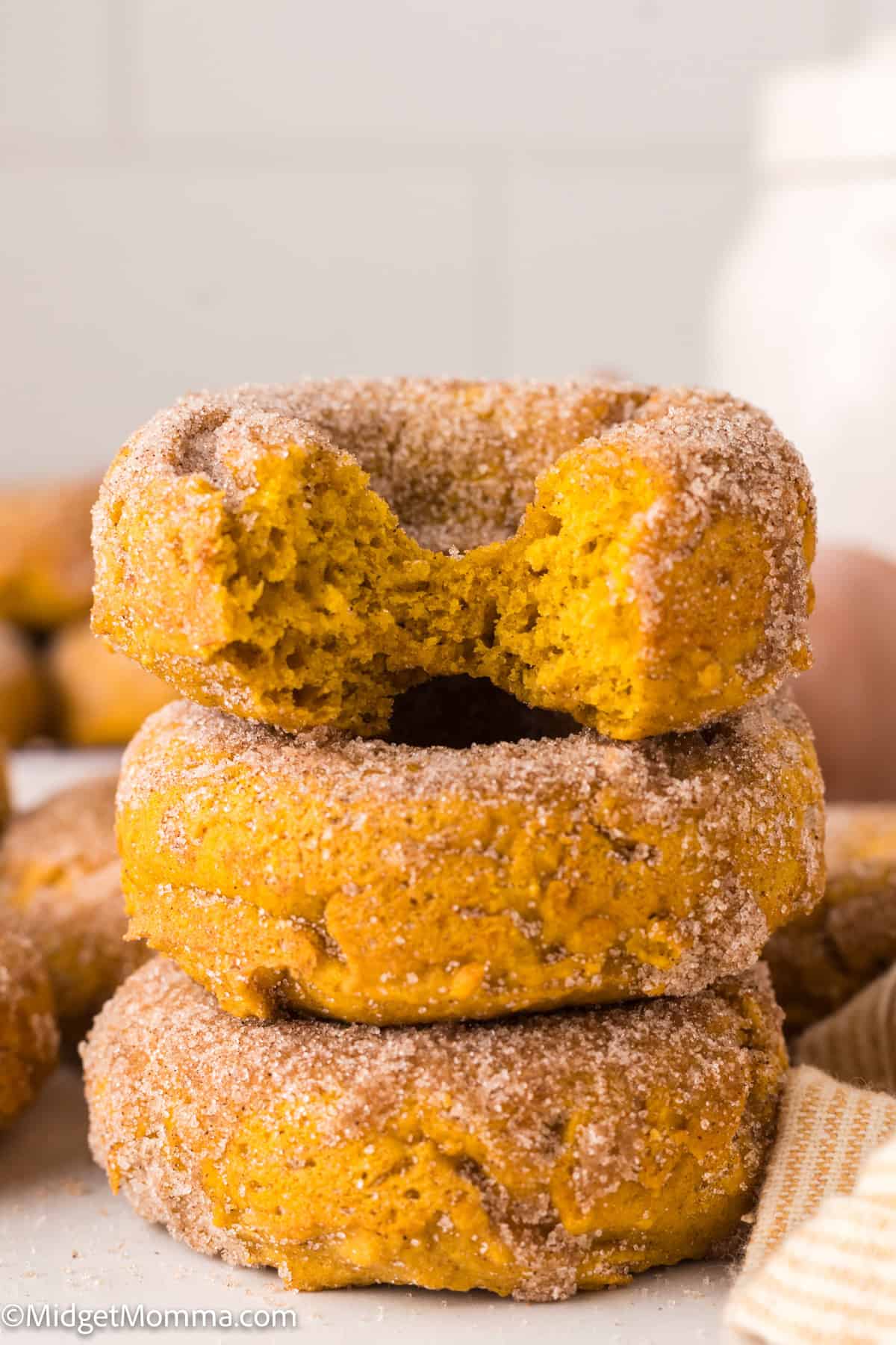 Three cinnamon sugar-coated donuts are stacked on top of each other, with the top donut showing a large bite taken out of it.