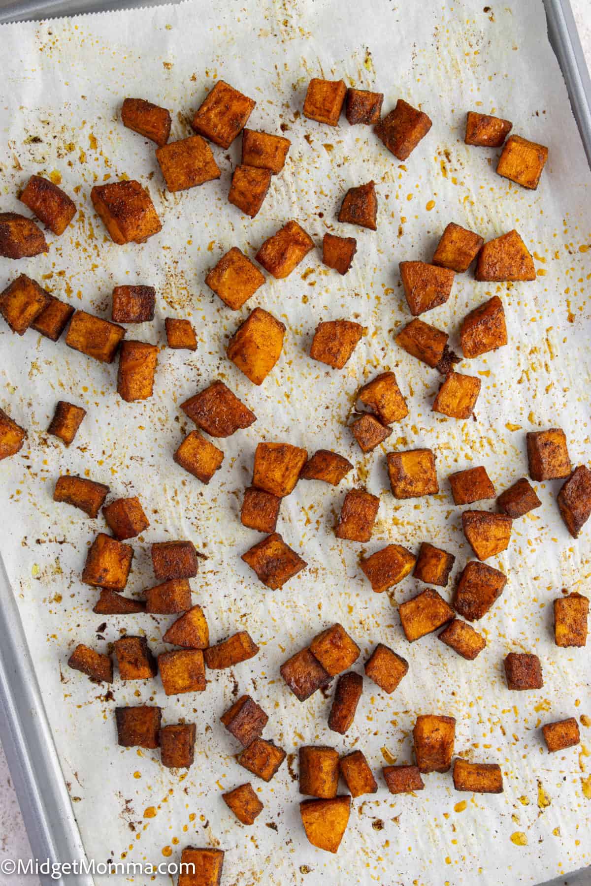 Cubed pieces of roasted sweet potato, seasoned and spread on a parchment-lined baking sheet.