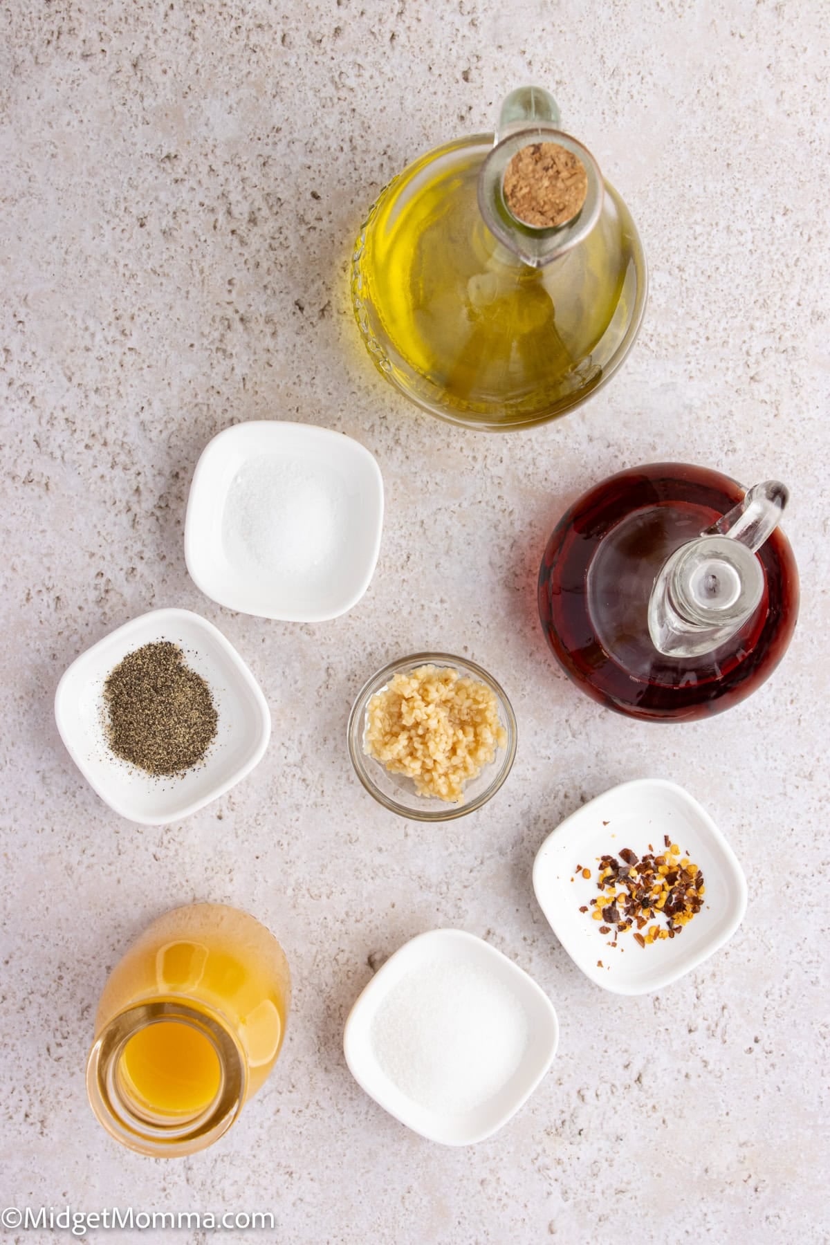 Assorted ingredients including olive oil, red wine vinegar, black pepper, salt, minced garlic, crushed red pepper, apple cider vinegar, and sugar in small bowls on a light surface.