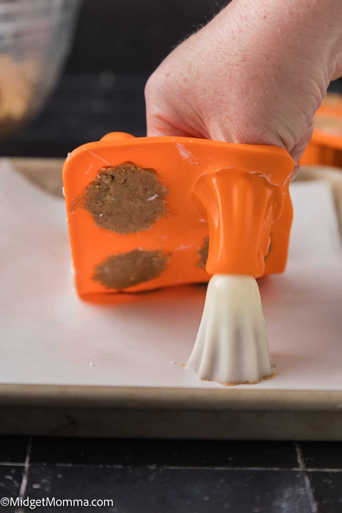 A hand holds an orange silicone mold with cookie dough,