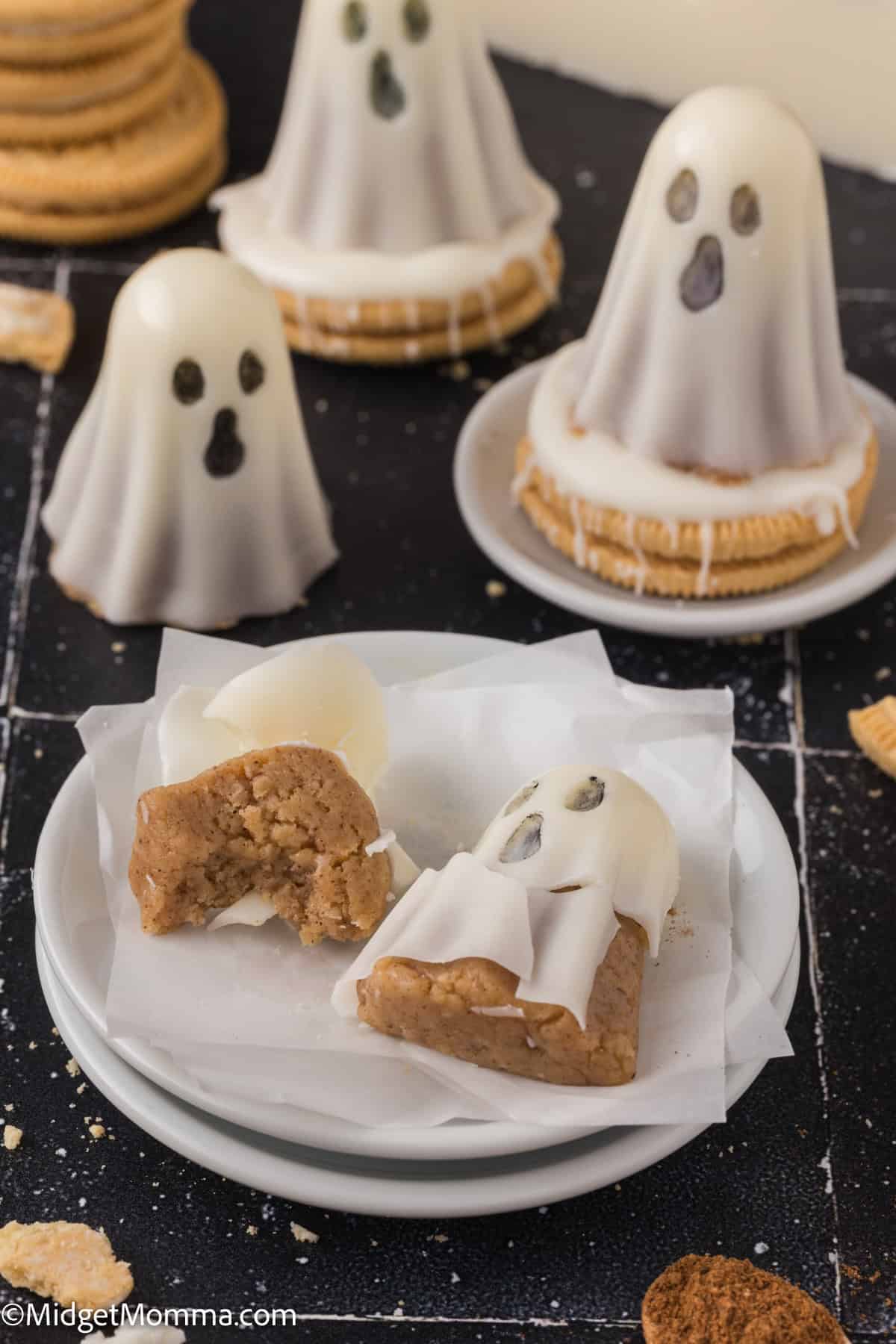 Several ghost-shaped treats made from cookies and white icing are displayed on plates, with one treat broken in half to show the inside.